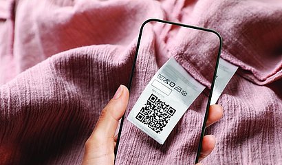 Handyscreen über Textilie mit Bild des QR-Codes auf der rosafarbenen Textilie